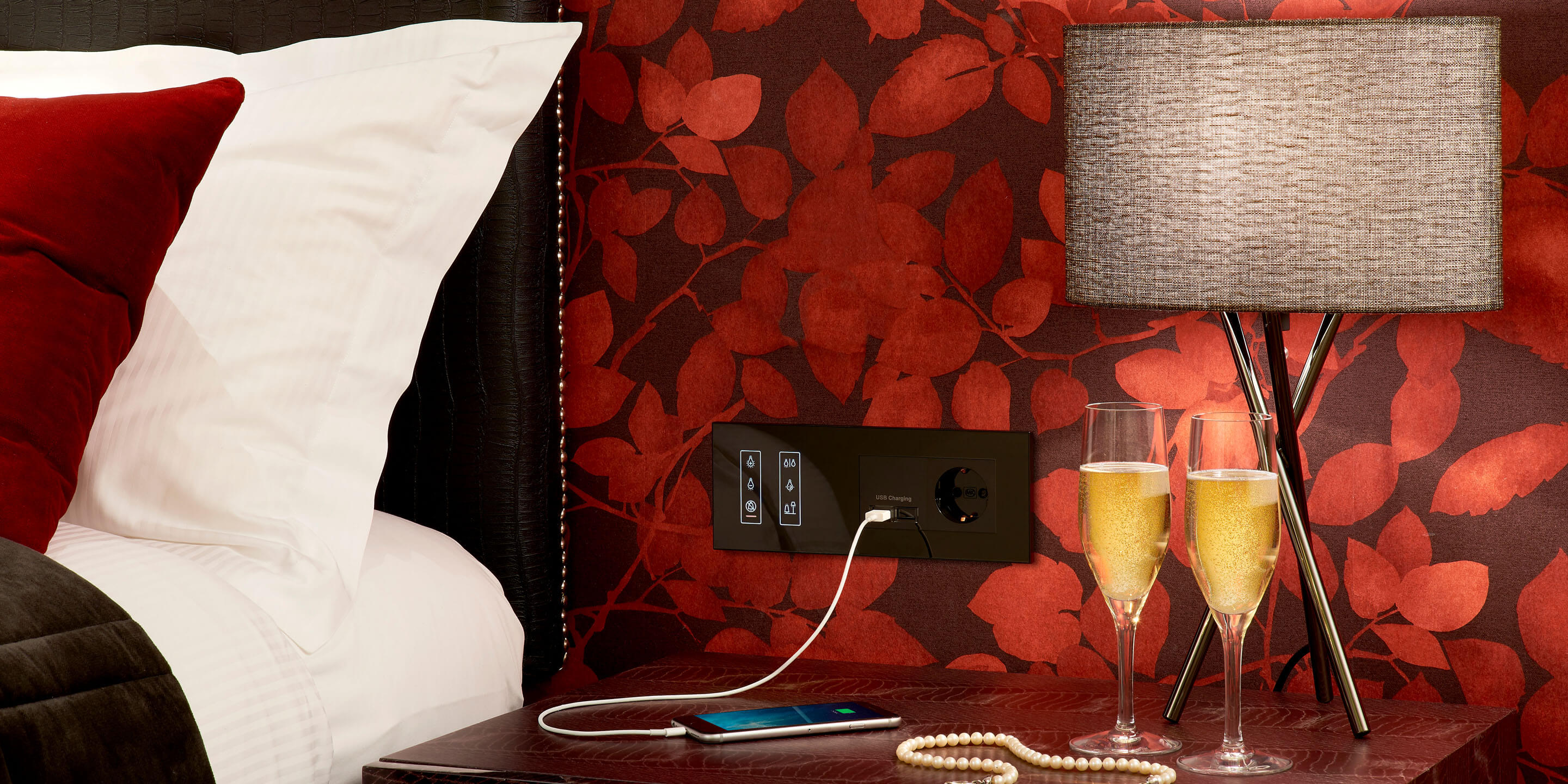 Black glass dimmer switch above bedside table in hotel room charging phone 