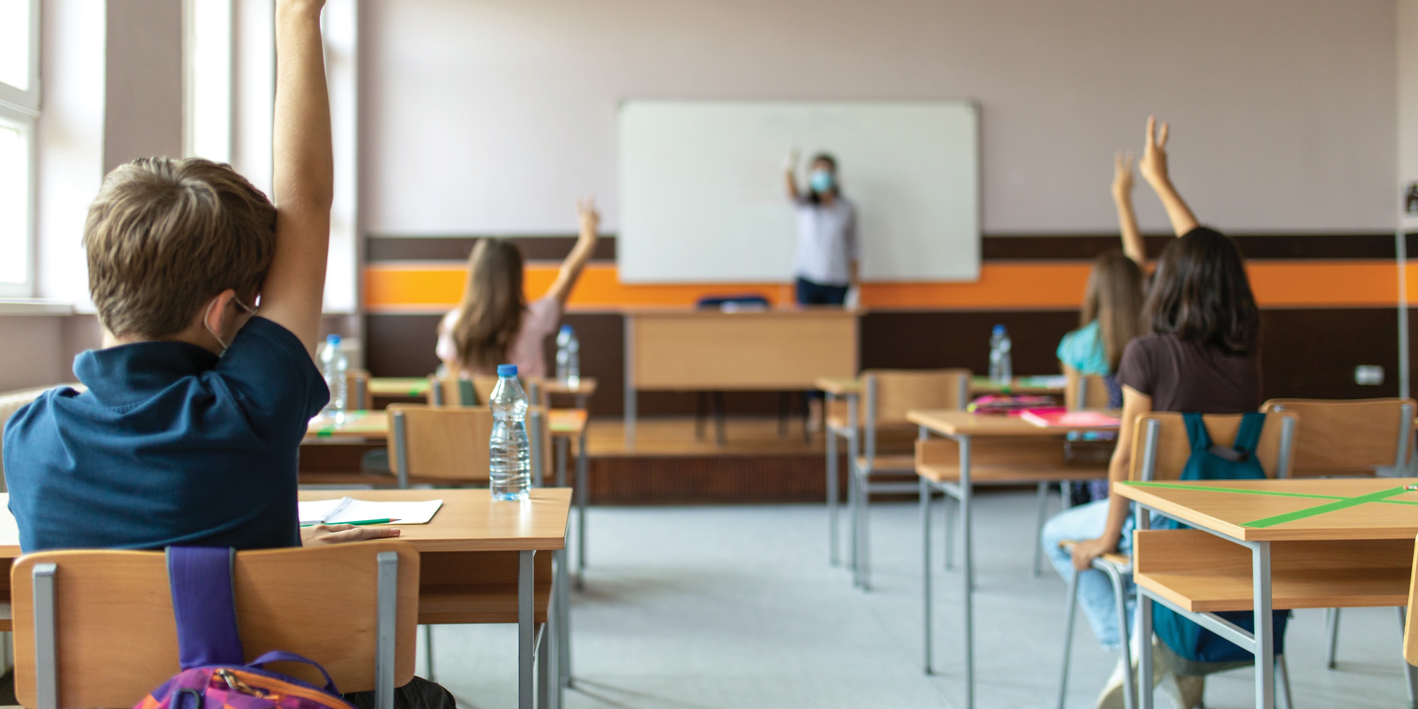Students raising hands in classroom.