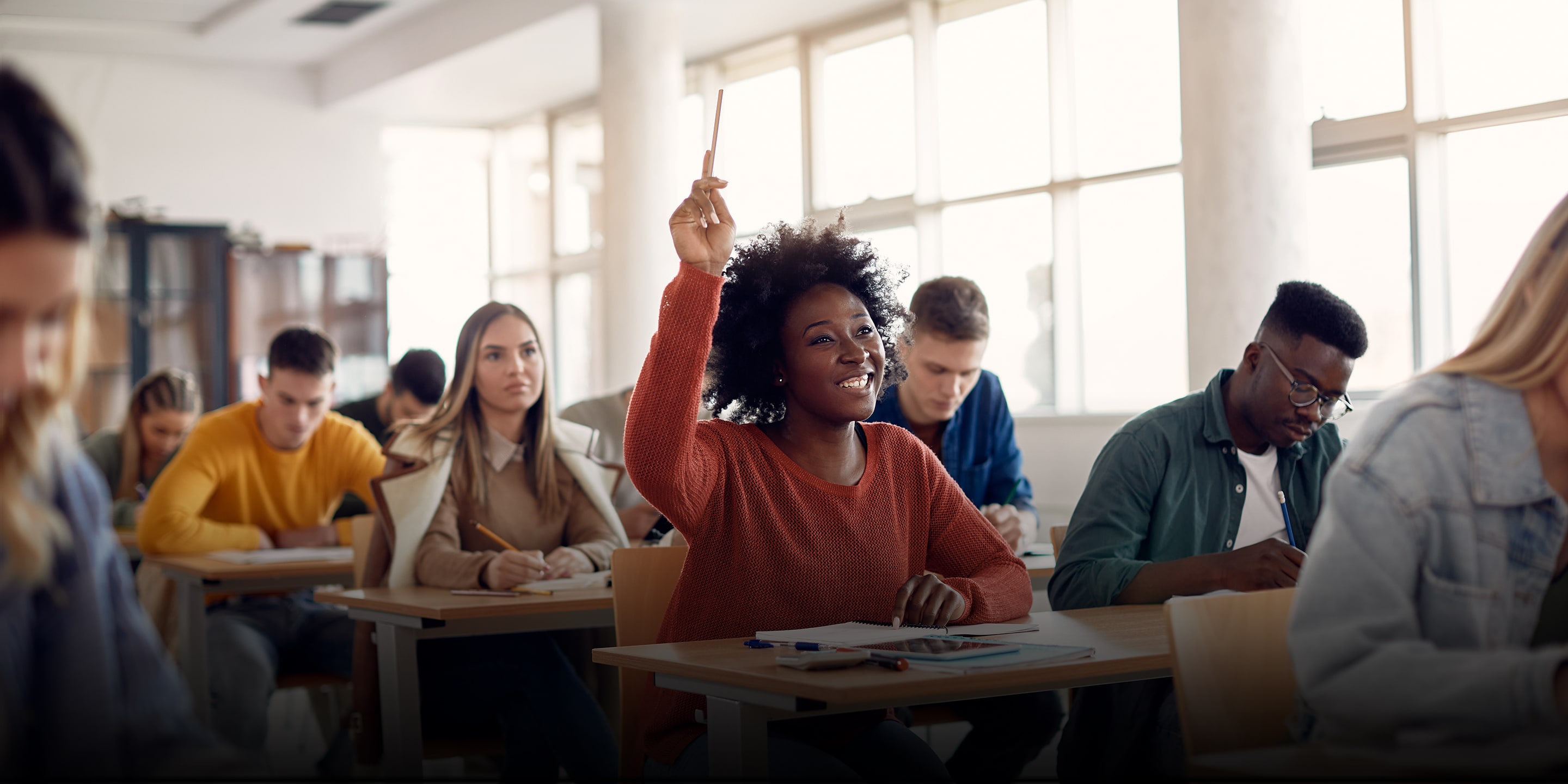 Happy African American student raising her hand to ask a question during lecture in the classroom. 