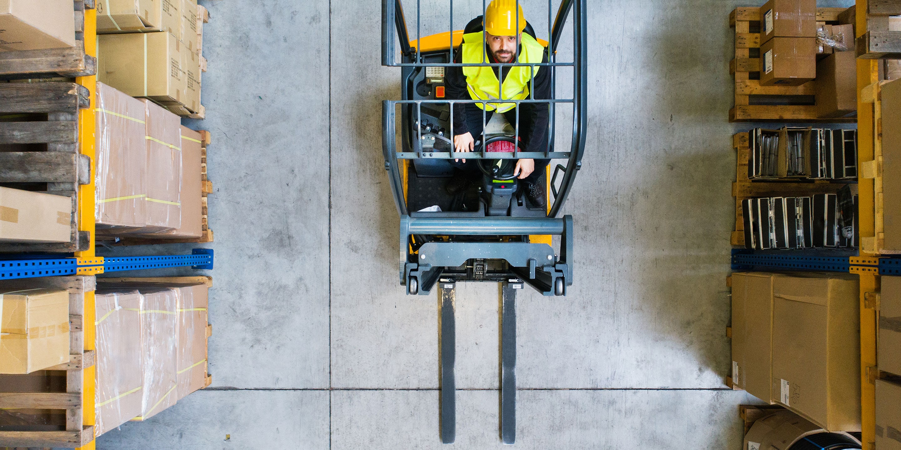 Worker in hard hat driving fork lift in warehouse