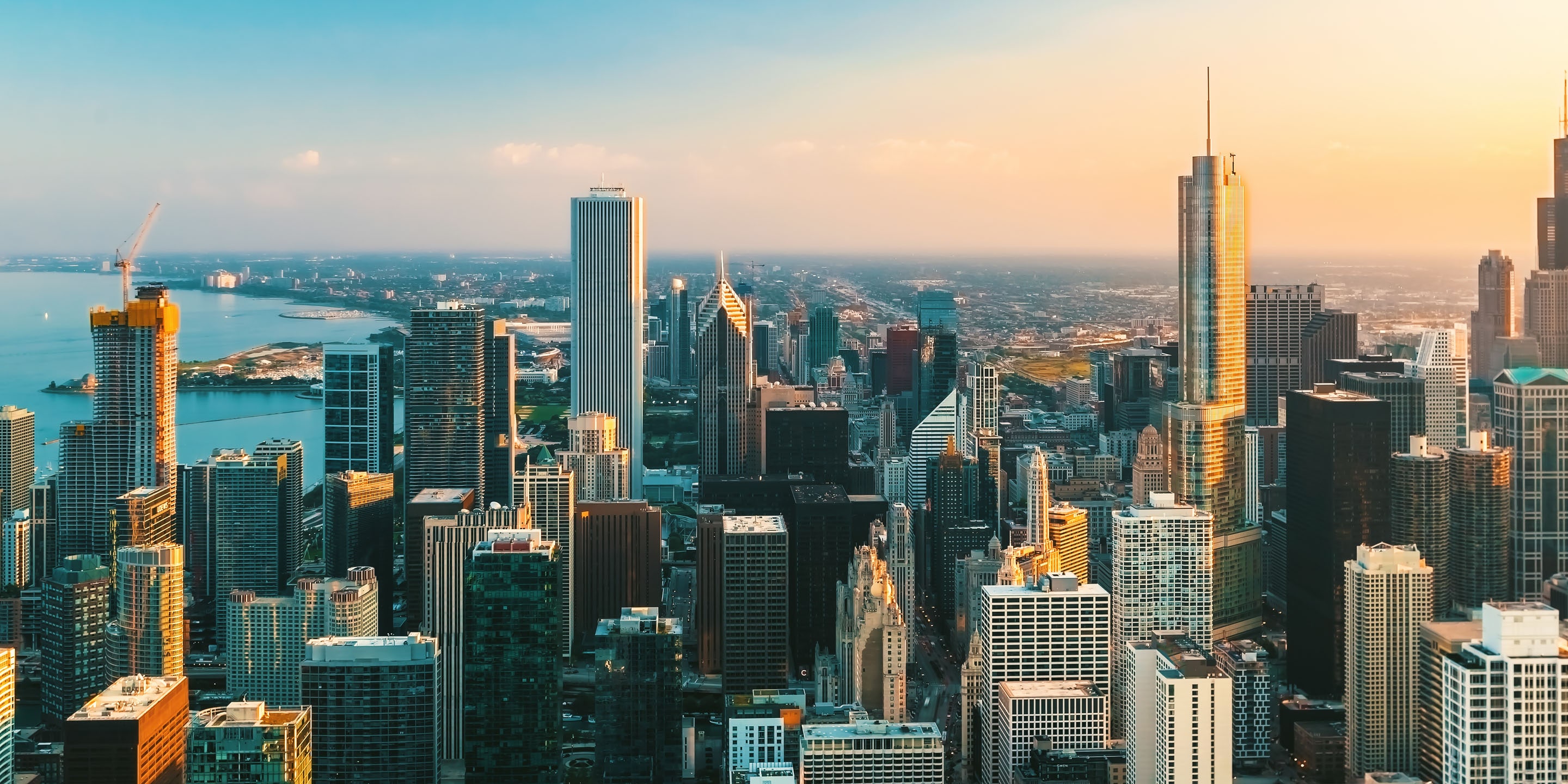 Tall buildings reflect sunset near lake and distant horizon.