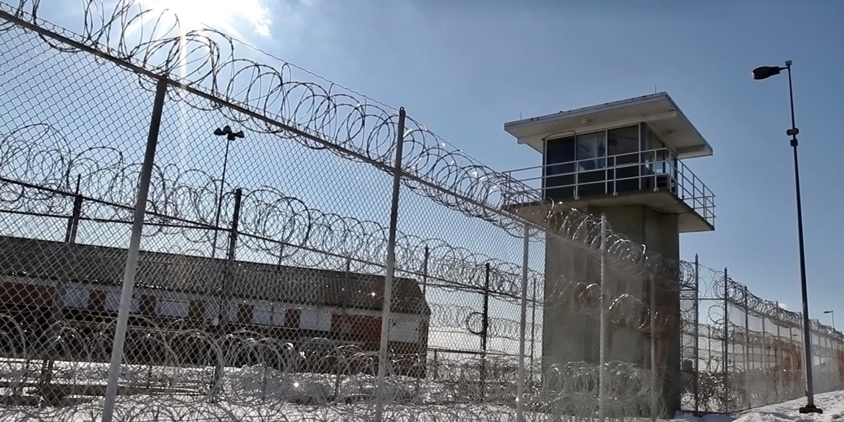 Barbed wire fence surrounds tower under clear sky, lights visible.