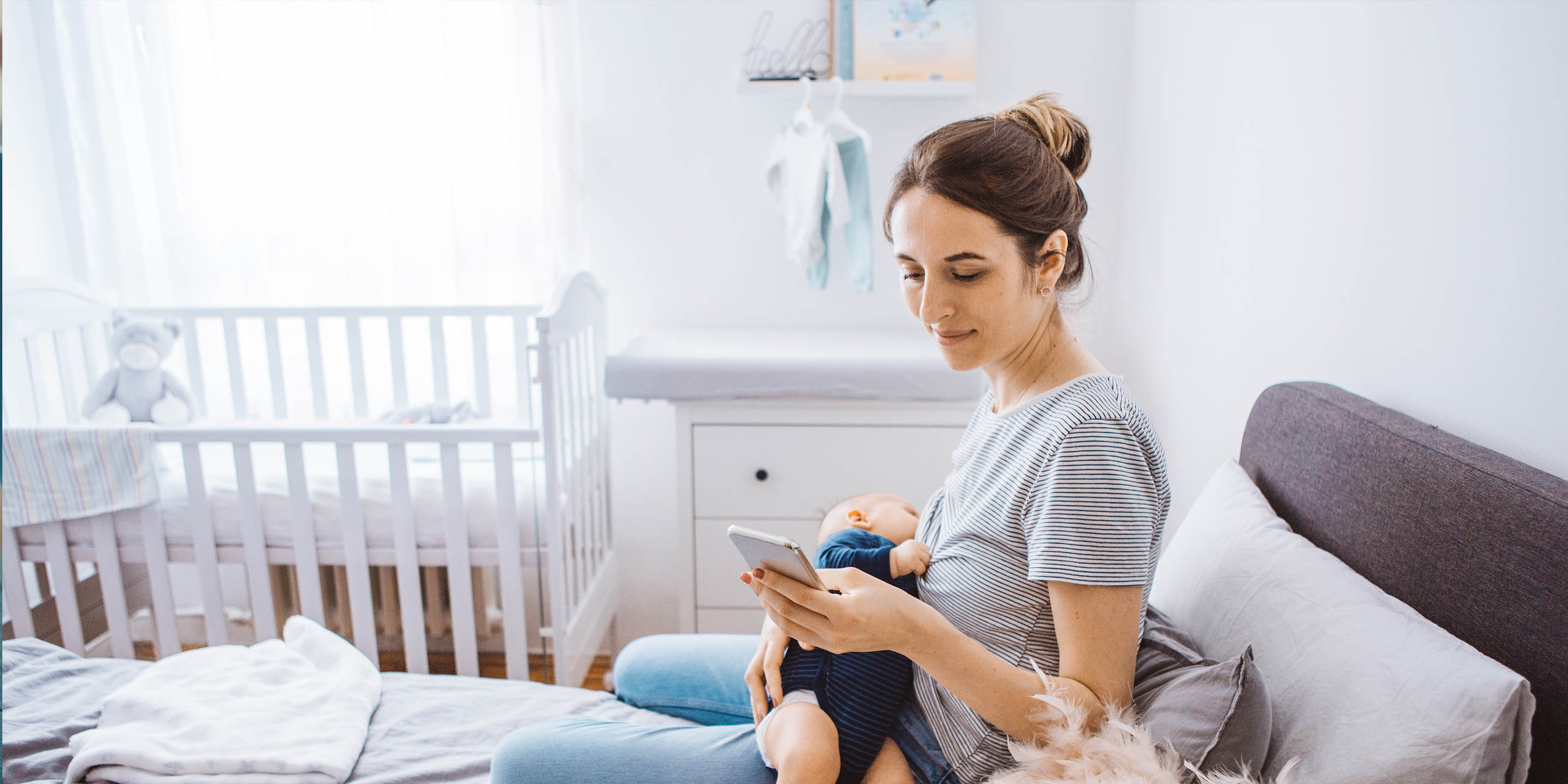 Mother holding baby and on phone in room with crib